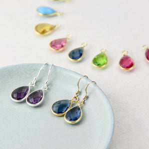 Sapphire earrings with gold hooks and Amethyst earrings with silver hooks displayed on a dish