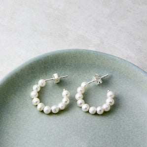 Pearl hoop huggie earrings with silver posts and backs shown on a dish