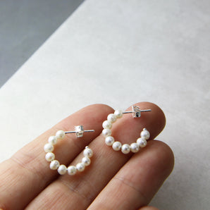 Pearl hoop huggie earrings with silver posts and backs shown against fingertips for size