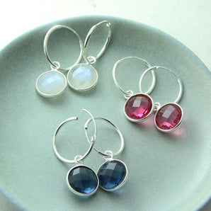 Moonstone, Ruby, and Sapphire semi-precious birthstone earrings with silver hoops shown arranged on a dish