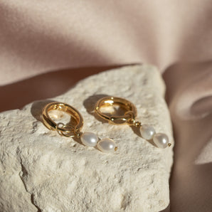 Two Pearl Drop Huggie Clicker Hoop Earrings displayed on a rock