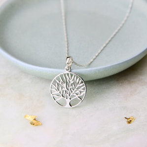 Round Tree of Life pendant on a silver chain propped up against the edge of dish