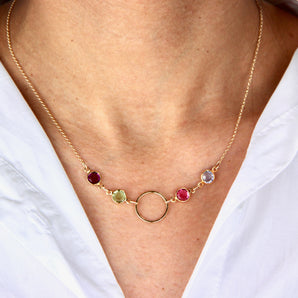 Gold necklace with four birthstones and circle pendant worn around a neck