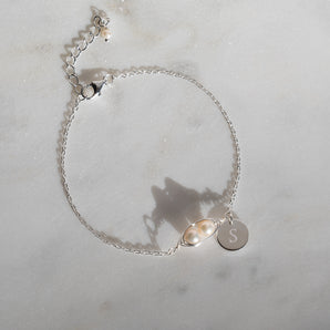 Sterling Silver And Pearl Peapod Bracelet with engraved 'S' disc charm displayed on a marble surface