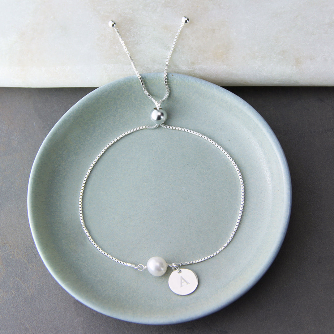 Silver pearl bracelet with engraved disc charm in a small dish