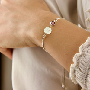 Silver bracelet with birthstone and initial charm worn around a wrist
