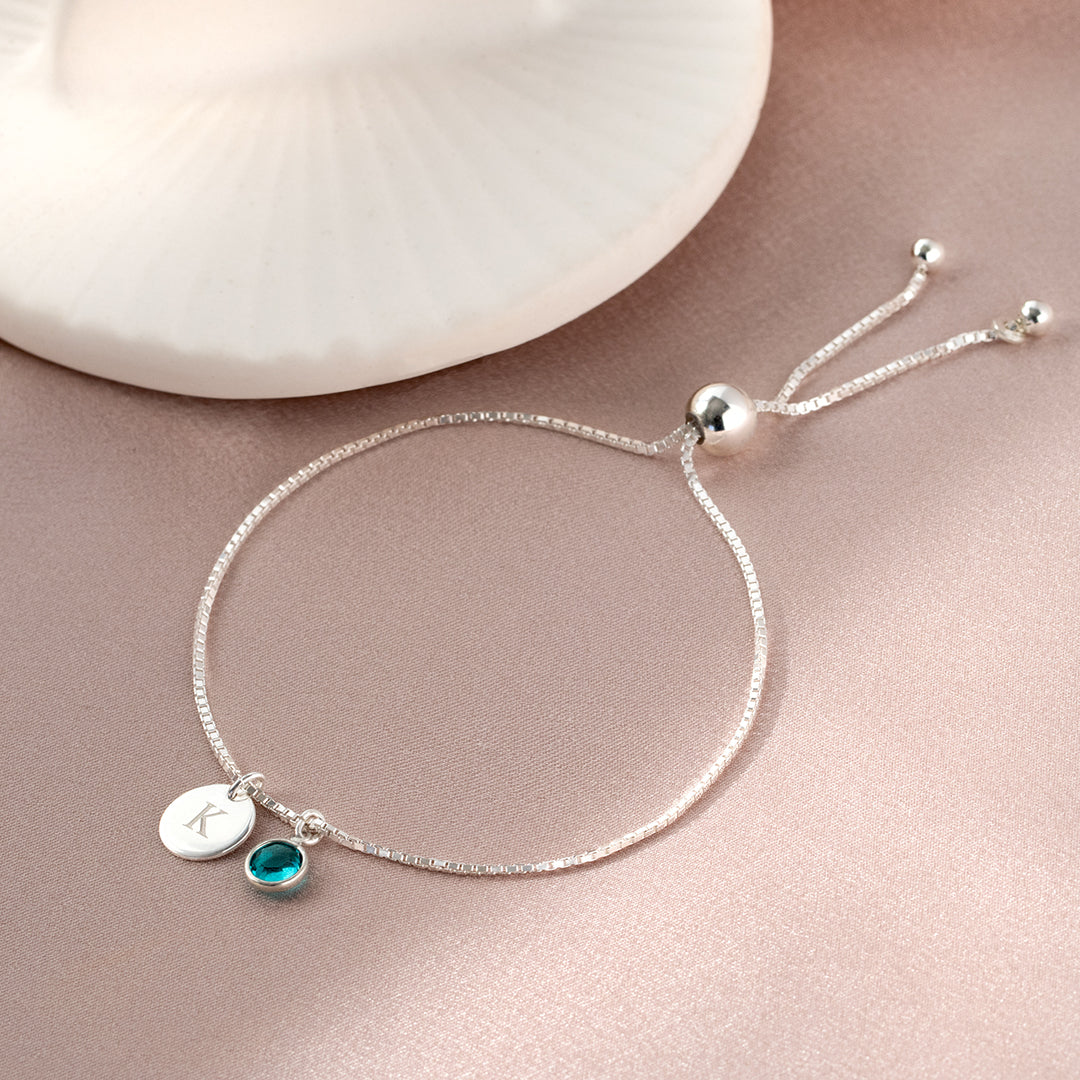 Silver adjustable bracelet with birthstone and engraved disc charm on a pale pink surface