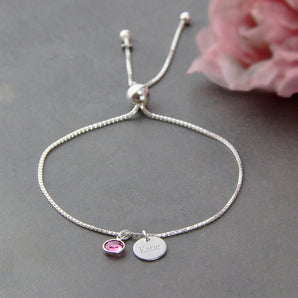 Silver adjustable bracelet with birthstone and engraved disc on a grey surface