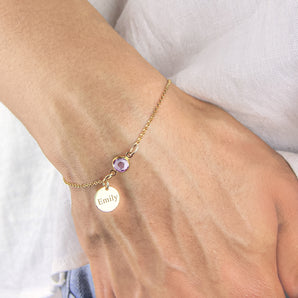 Gold bracelet with pale amethyst birthstone and engraved disc charm worn around a wrist