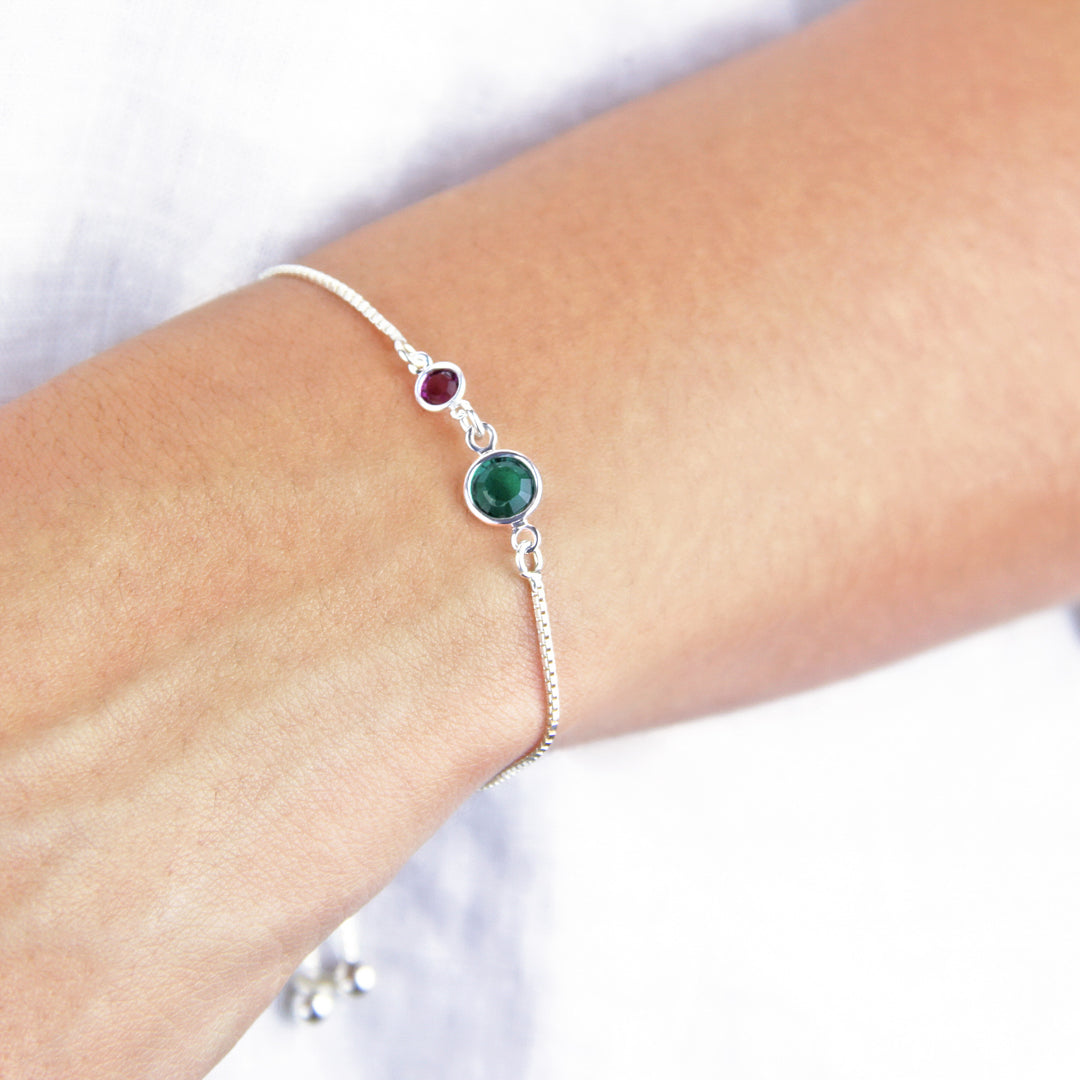 Adjustable silver bracelet with emerald and amethyst birthstones worn around a wrist