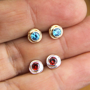 Silver and gold birthstone nest studs shown against finger tips for size