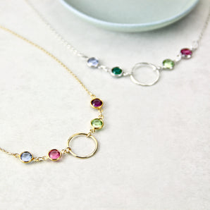 Gold and silver necklaces each with four birthstones and circle pendants on a white background