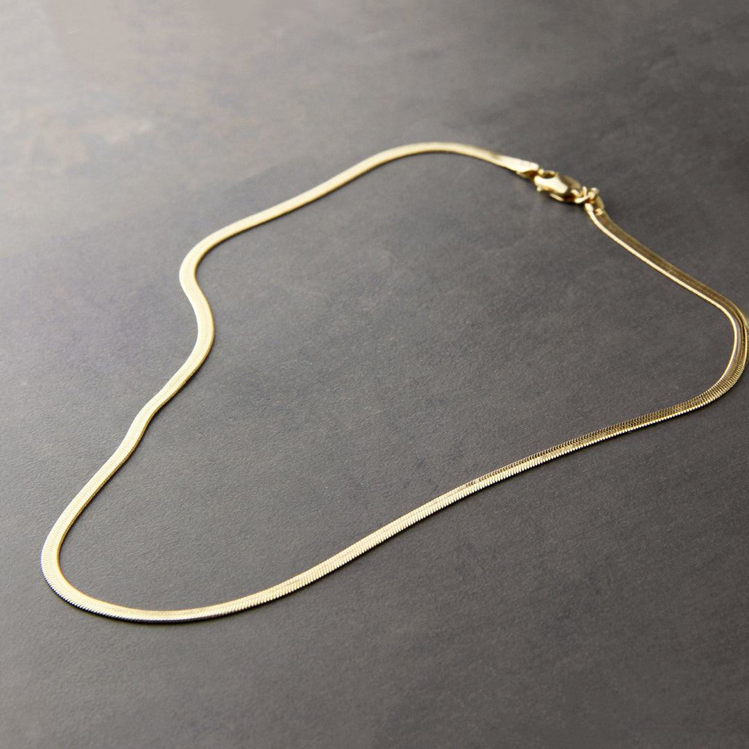 Gold snake herringbone necklace on a grey background