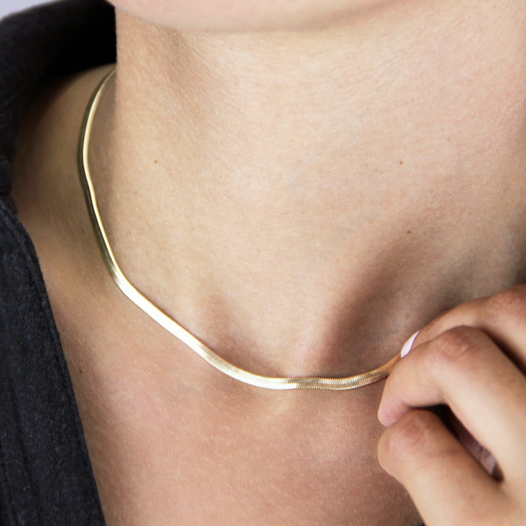 Gold snake herringbone necklace worn around the neck of a model
