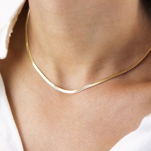 Gold snake herringbone necklace worn around the neck of a model