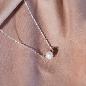 Silver pearl necklace on pink surface